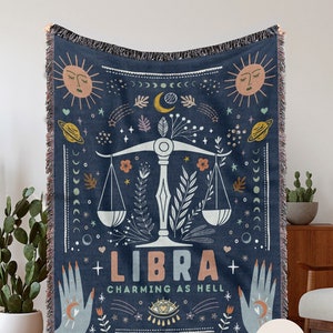 May include: A blue woven throw blanket with a Libra zodiac sign and the text "Charming as Hell". The design features a scale, stars, moons, and other celestial symbols.