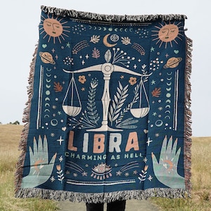 May include: A blue woven tapestry with a Libra zodiac symbol and the text "Libra Charming as Hell". The tapestry features a scale, stars, and moons.