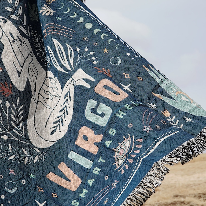 May include: A blue woven throw blanket with a white and pink illustration of a Virgo zodiac sign and the text "SMART AS HELL".