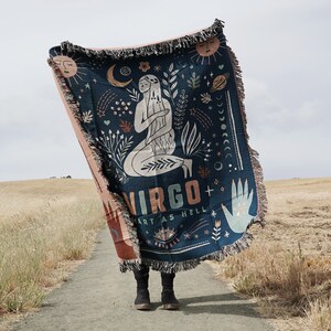 May include: A blue and pink woven tapestry with a graphic design of a woman with long hair, surrounded by stars, moons, and the word "VIRGO" with the text "ART AS HELL" below.