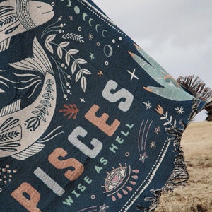 May include: Dark blue woven throw blanket with a Pisces design. The blanket features a large fish illustration, celestial elements, and the words "PISCES WISE AS HELL" in a mix of colors. The edges have a fringe.