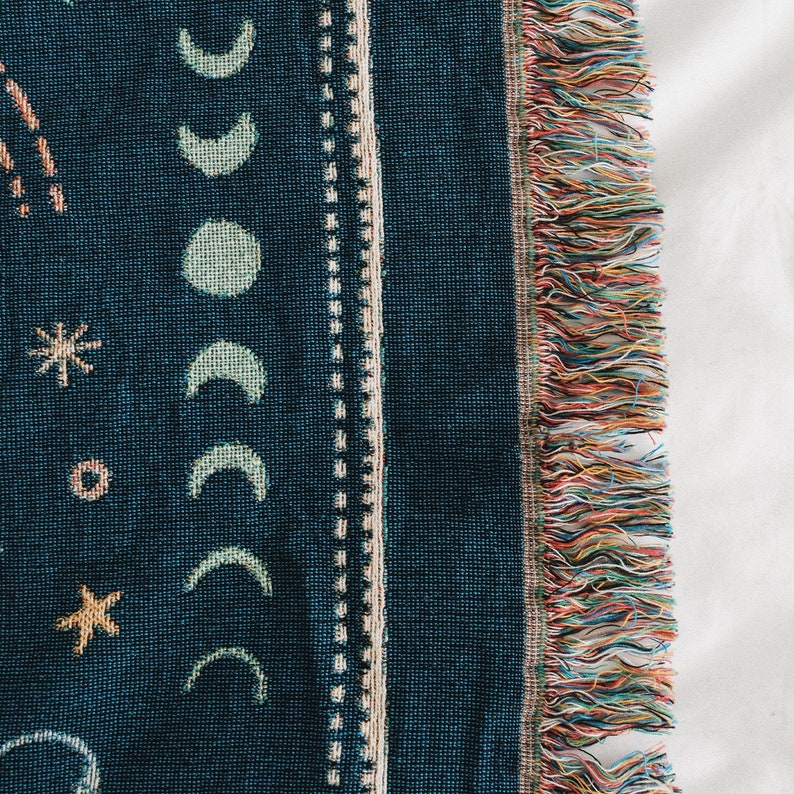 May include: A dark blue woven throw blanket with a fringe border. The blanket features a pattern of stars, moons, and other celestial designs.