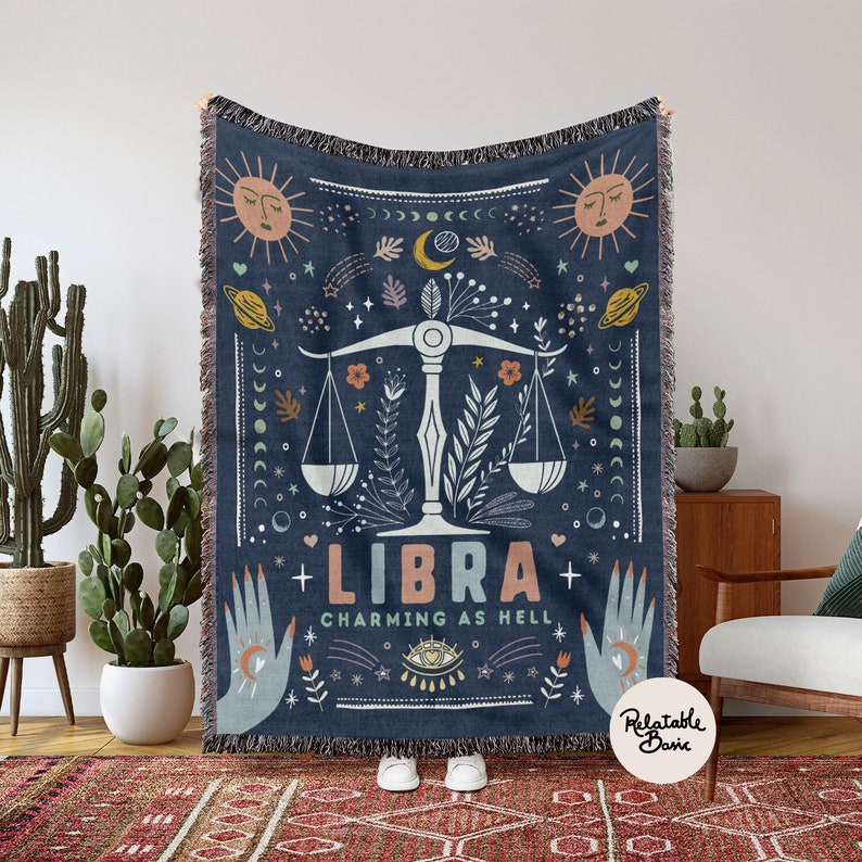 May include: A blue woven throw blanket with a Libra zodiac sign and the text "Charming as Hell". The design features a scale, stars, moons, and other celestial symbols.