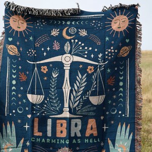 May include: A blue woven tapestry with a Libra zodiac sign and the text "CHARMING AS HELL". The tapestry features a scale, stars, moons, and other celestial imagery.