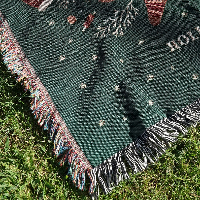 May include: Green woven throw blanket with a fringe border. The blanket features a white snowflake pattern and the word "Home" in white lettering.