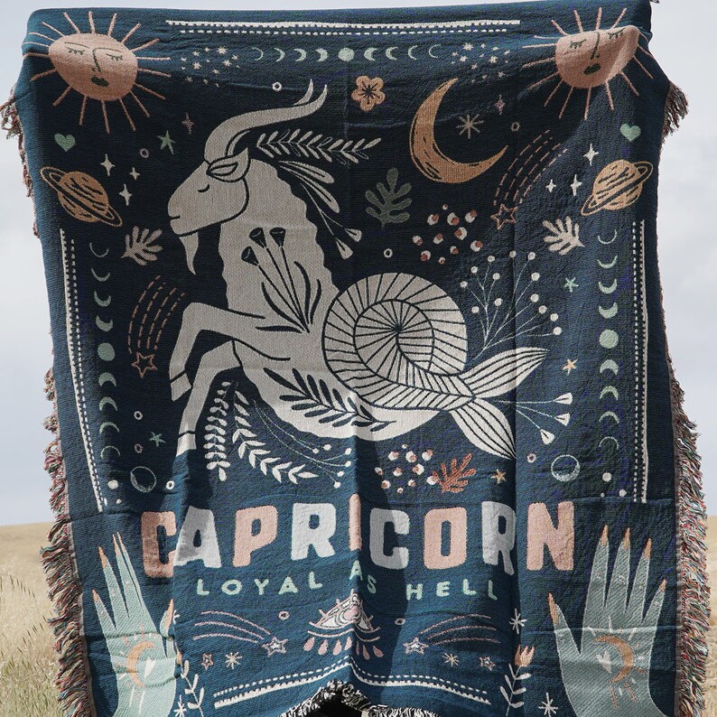 May include: Dark blue woven throw blanket featuring a Capricorn zodiac design. The blanket displays a goat illustration, celestial elements, and the words "CAPRICORN LOYAL AS HELL" in a stylized font. The edges have a fringed trim.