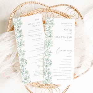 Op de afbeelding: Twee huwelijksceremonieprogramma's met bloemaccenten. De programma's zijn lichtgroen en wit, met de tekst "The Wedding Party" en "Welcome to the Wedding of Kate and Matthew". De programma's worden gepresenteerd op een gevlochten dienblad.