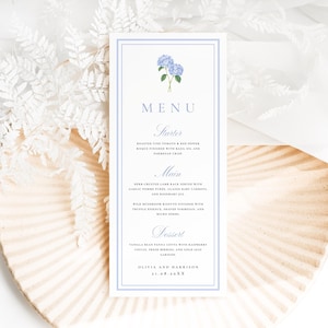 May include: A vertical rectangular menu card with a light blue double-line border and a blue hydrangea illustration at the top. The text lists courses including Starter, Main, and Dessert, ending with the names Olivia and Harrison and the date 21.08.20XX.