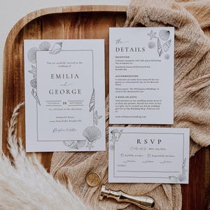Puede incluir: Juego de invitaciones de boda con temática de conchas marinas. La invitación, los detalles y las tarjetas RSVP están dispuestos en una bandeja de madera con una tela neutra. La invitación incluye los nombres "EMILIA y GEORGE" y la fecha "25 SEPTIEMBRE".
