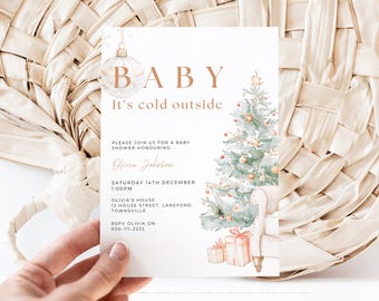 May include: A white card with a gold and white ornament and a watercolor illustration of a Christmas tree. The text on the card reads "BABY It's cold outside" and includes details for a baby shower.