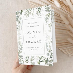 Może przedstawiać: Złożony program ślubny z kwiatowym wzorem. Program zawiera tekst „WELCOME TO THE WEDDING OF OLIVIA and EDWARD” oraz datę i miejsce ślubu. Program jest ozdobiony zielonymi i białymi liśćmi.