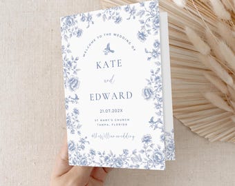 May include: A white wedding invitation with a blue floral border. The text reads "Welcome to the wedding of Kate and Edward 21.07.202X St Mary's Church Tampa, Florida #thewilliamwedding"