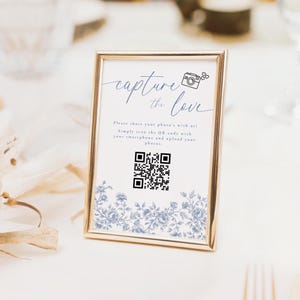 May include: A white sign with a gold frame and a blue floral pattern. The sign says "capture the love" and has a QR code and a camera icon.