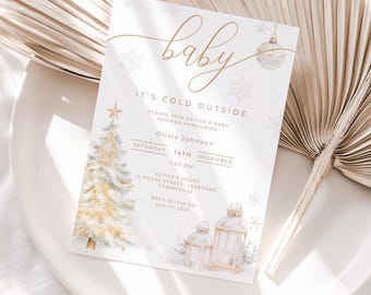 May include: A baby shower invitation with a winter theme. The invitation features the word "baby" in elegant gold script, along with the text "It's Cold Outside." A Christmas tree and lanterns are illustrated in soft watercolor tones.