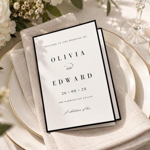Könnte beinhalten: Eine rechteckige Hochzeits-Programmkarte mit schwarzem Rand auf weißem Hintergrund. Der Text lautet: WELCOME TO THE WEDDING OF OLIVIA and EDWARD 26 08 28 THE HARRINGTON ESTATE A celebration of love. Die Karte ist gefaltet und zeigt eine schwarze Serifenschrift.