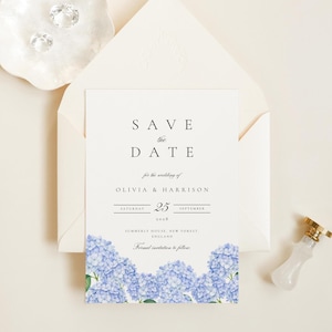 May include: A white Save the Date card with blue hydrangea flowers at the bottom. The card includes the text "SAVE the DATE" and details for the wedding of Olivia & Harrison, set for September 25, 2028. An envelope and wax seal are also visible.