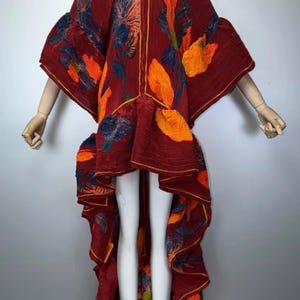 May include: A deep red pleated dress featuring a V-neckline and wide, flowing sleeves. The garment is adorned with a vibrant floral pattern in shades of bright orange and dark blue. It has a high-low hemline with ruffled edges and yellow trim.