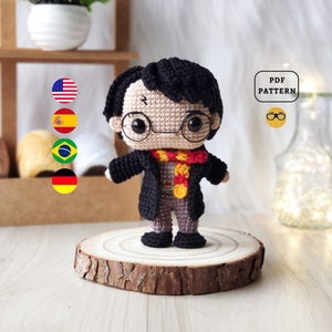 Può includere: Bambola amigurumi all'uncinetto di Harry Potter, con una tunica nera, una sciarpa rosso e gialla e occhiali rotondi. La bambola è in piedi su una fetta di legno. L'immagine include il testo "PDF PATTERN".