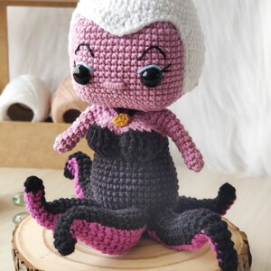 May include: A crocheted amigurumi doll of Ursula from The Little Mermaid. The doll is purple with a white crocheted hat and black and pink crocheted tentacles.