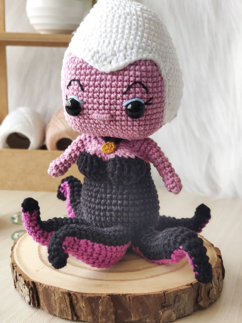 May include: A crocheted amigurumi doll of Ursula from The Little Mermaid. The doll is purple with a white crocheted hat and black and pink crocheted tentacles.