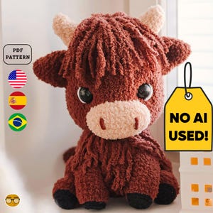 May include: A handmade, plush Highland cow with a shaggy, reddish-brown coat, cream-colored horns, and a light tan muzzle. The cow has large, black eyes and is sitting. A yellow tag reads "NO AI USED!" and a "PDF PATTERN" label is visible.