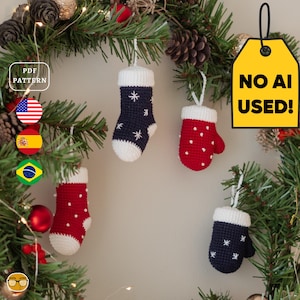 May include: Four crocheted Christmas ornaments hanging from a pine branch: two red mittens with white dots, one navy blue stocking with white star patterns, and one navy blue mitten with white star patterns, all featuring white cuffs and hanging loops.