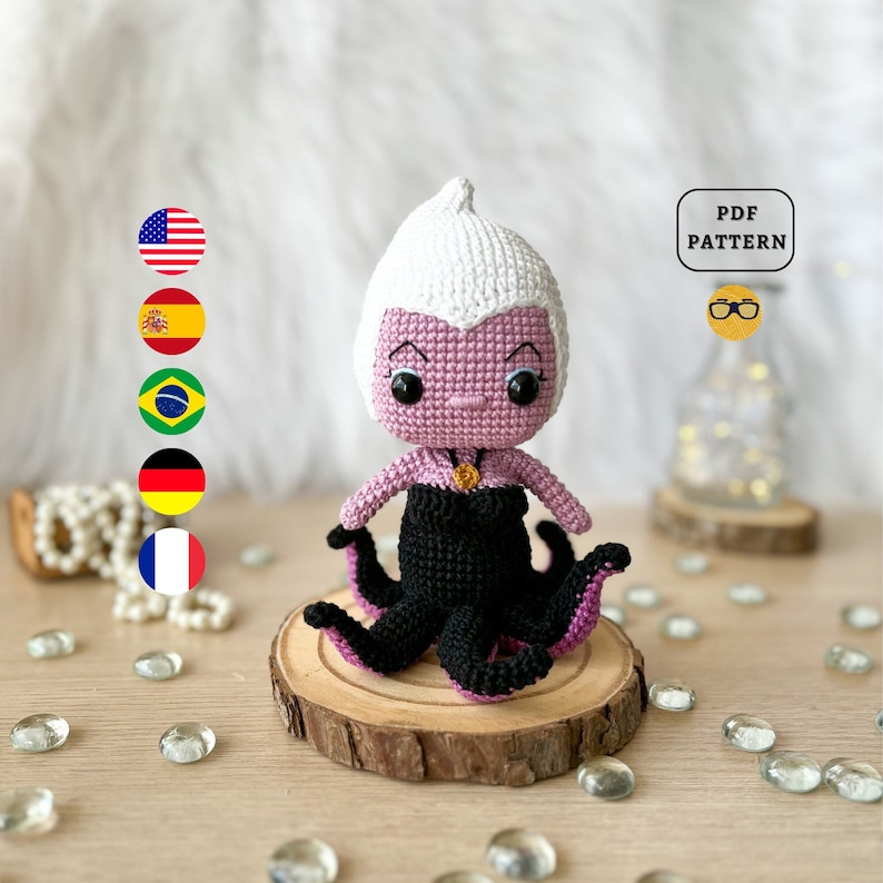 May include: Crocheted amigurumi doll of Ursula from The Little Mermaid. The doll is purple with a white crocheted hairpiece and black crocheted tentacles. The doll is wearing a black dress and a gold necklace. The doll is sitting on a wooden base. The image includes the text "PDF PATTERN".