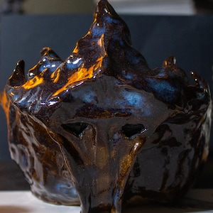 Peut inclure: Un bol en céramique fait à la main avec une forme organique unique. Le bol présente un glaçage brillant dans les tons de marron, de bleu et d'or, créant un aspect texturé et fondu. Le design a une forme de montagne, avec des pics et des vallées.