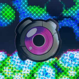 May include: A round, gray and silver sticker with a pink eye in the center. The eye has a black pupil and a white ring around it.