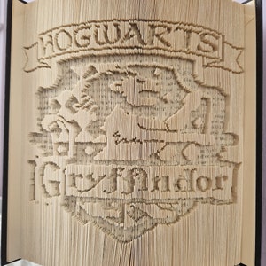 Puede incluir: Un libro con el escudo de Hogwarts y las palabras "Hogwarts" y "Gryffindor" plegadas en un diseño 3D.