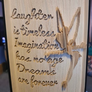 May include: A book art sculpture with a fairy design and the text "Laughter is timeless, Imagination has no age, Dreams are forever".