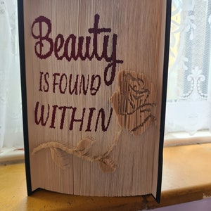 May include: A book art sculpture with a rose design and the text "Beauty is found within".