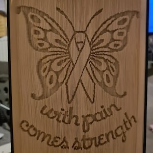 May include: A book art sculpture of a butterfly with a ribbon in the center. The sculpture is made of folded pages and has the text "with pain comes strength" at the bottom.