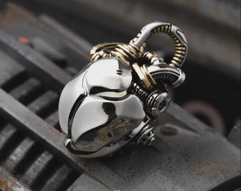 May include: A silver pendant with a futuristic, mechanical design. The pendant has a rounded, segmented body with gold-colored accents and a loop for a chain. The overall aesthetic is reminiscent of science fiction or steampunk.