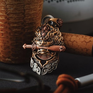 May include: A gold and silver pendant featuring a detailed lion's head with a sword in its mouth. The pendant has intricate details and a textured surface.