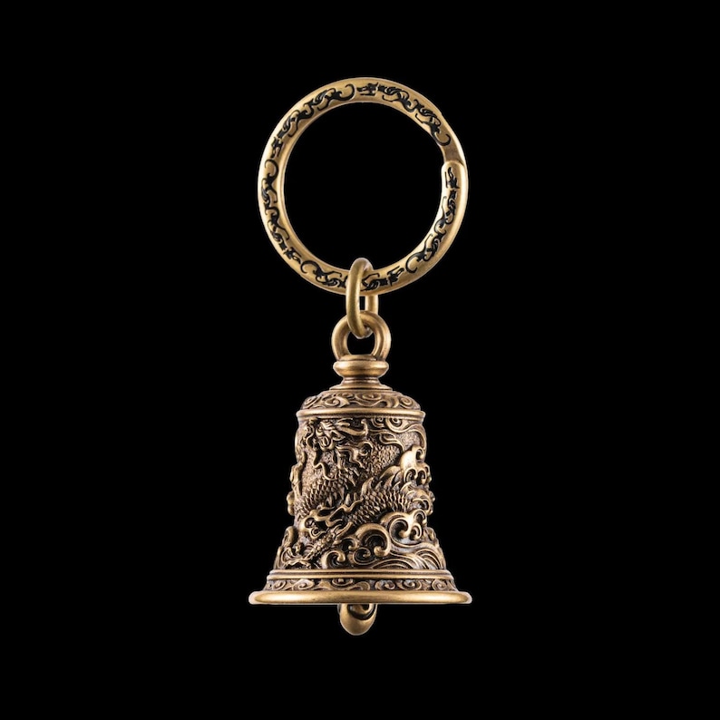 May include: A detailed brass bell keychain with a dragon motif. The bell is suspended from a decorative ring. The bell's surface features intricate carvings of dragons and waves, with a dark background.
