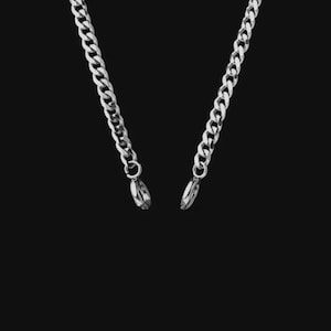 Puede incluir: Un collar de cadena de metal en tono plateado con un diseño de eslabones tipo barbada. Los dos extremos de la cadena cuelgan hacia abajo, terminando cada uno en un pequeño anillo conector circular de metal pulido con acabado brillante.