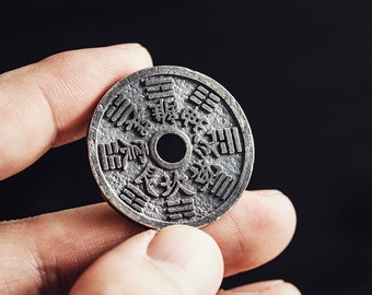 May include: A silver-colored coin with Chinese characters and a circular design. The coin is being held in a hand.