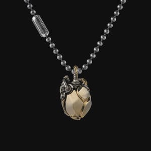 May include: A silver-toned ball chain necklace featuring a mechanical heart pendant. The pendant combines polished gold-toned and oxidized silver-toned metal components, showcasing intricate pipes, gears, and valves in a complex, layered design.
