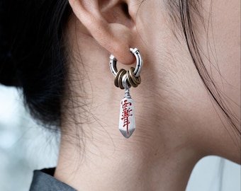 May include: A silver-toned hoop earring featuring three small bronze-colored rings suspended from the hoop. A silver-toned, shield-shaped pendant hangs from the rings, displaying red engraved Chinese characters on its front surface.