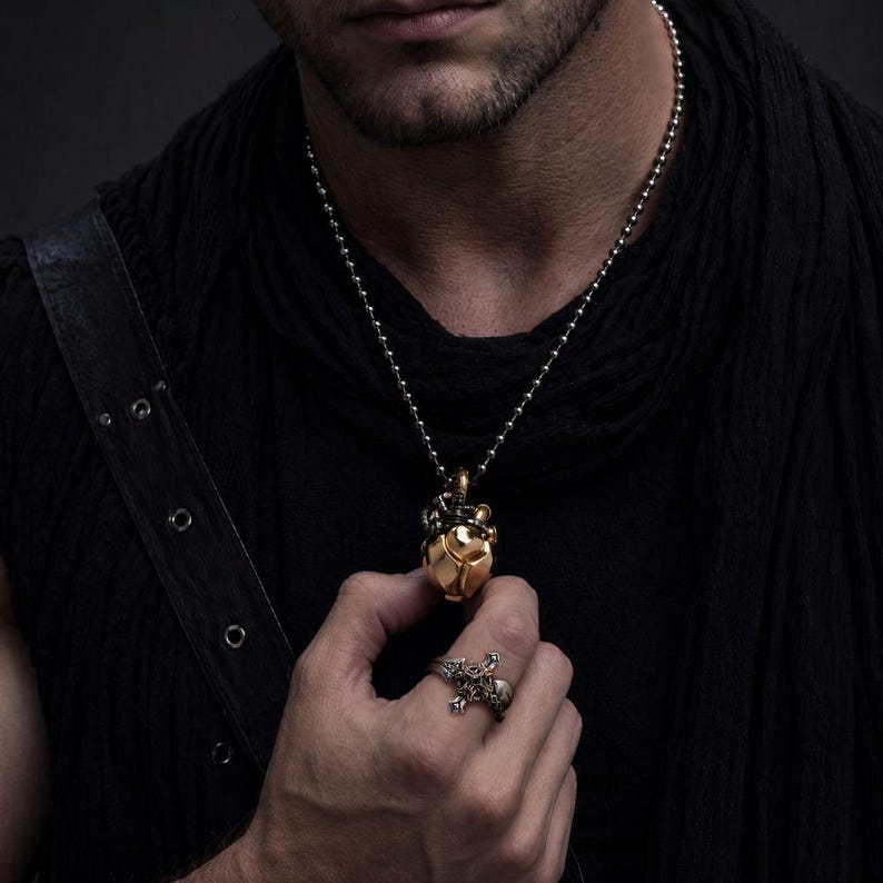 May include: A gold-toned heart-shaped pendant with intricate mechanical detailing suspended from a silver-toned ball chain necklace, paired with a silver-toned ring featuring a detailed cross design with ornate metalwork and small embedded stones.