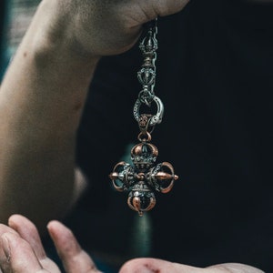 May include: A silver and copper pendant with a detailed design. The pendant is shaped like a cross with four arms that have intricate details. The pendant is hanging from a silver chain.