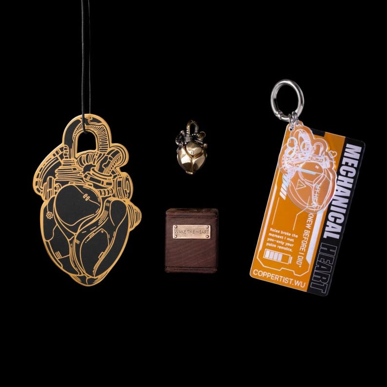 May include: A black and gold anatomical heart pendant on a cord, a small metallic heart charm, a brown box with a metal plate reading WAKE THE HEART, and an orange rectangular keychain with the text MECHANICAL HEART and COPPERTIST.WU.