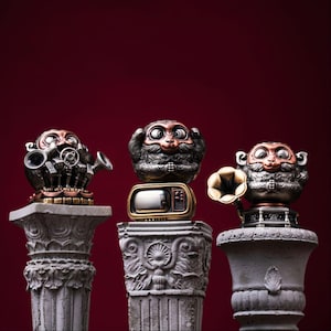 Könnte beinhalten: Drei metallische Affenfiguren in Kupfer- und Silbertönen, die jeweils auf einem grauen, steinartigen Sockel stehen. Ein Affe hält Mikrofone, ein anderer sitzt auf einem Vintage-Fernseher und der dritte steht neben einem Grammophontrichter.