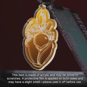 May include: A translucent amber-colored acrylic keychain featuring a white line-art illustration of a mechanical heart. The design includes intricate pipes and valves, suspended from a metal ring. The item has a protective film on both sides.