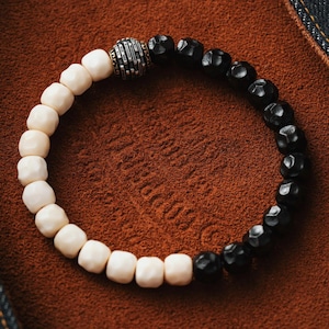 May include: A black and white beaded bracelet with a silver charm. The bracelet is made of two different types of beads, one black and one white. The charm is a silver sphere with a textured design.