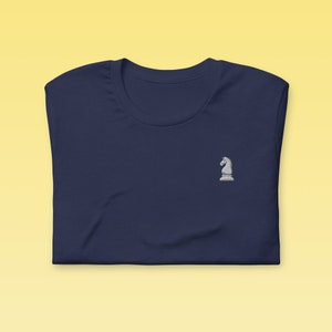 May include: A navy blue t-shirt with a white embroidered chess knight on the left chest.