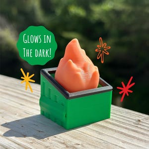 May include: A green miniature dumpster with a black rim contains an orange, flame-shaped object. The text "GLOWS IN THE DARK!" is in a green circle. Decorative orange and red starbursts are also present.