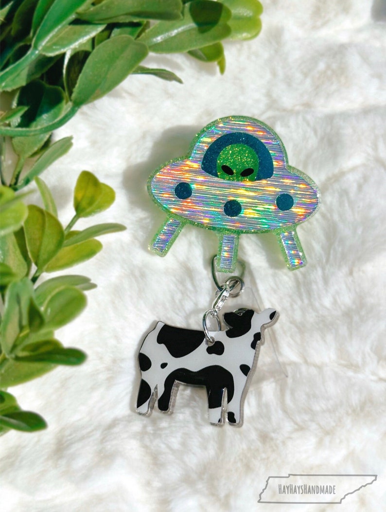 Insignia retráctil original con diseño de ovni, extraterrestre y abducción de vacas. Brilla en la oscuridad. Ideal para rellenar medias navideñas. Obsesionado con los extraterrestres.