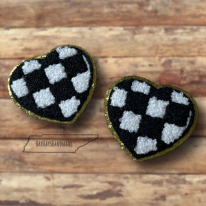 May include: Two black and white checkered heart-shaped patches with gold glitter trim. The patches are on a wooden background.